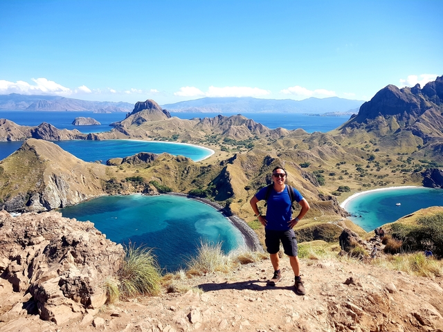       Man posing on a mountaintop with a view of the Komodo islands.
  