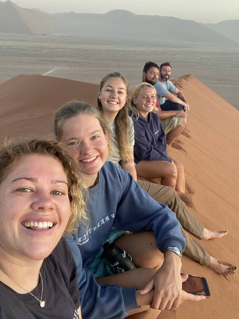       Group of people sitting on a sandy landscape.
  