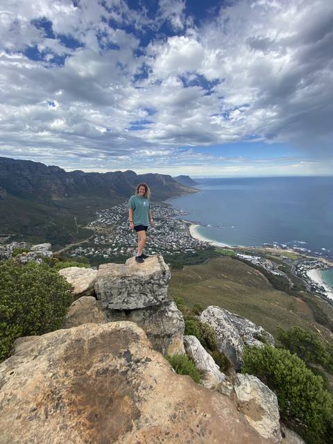       Person standing on a rocky outcrop overlooking a coastal city.
  