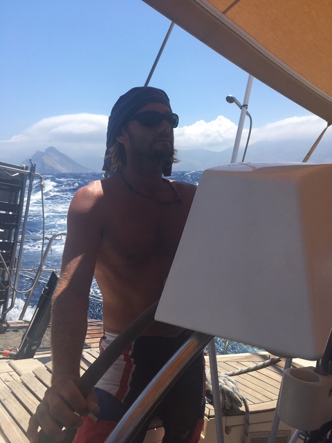 Man steering a boat with rough waters behind him.