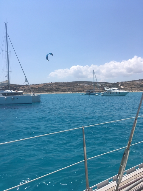 Multiple yachts on a blue sea with a sandy shore in the distance.