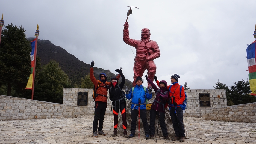 Group of hikers posing cheerfully in front of a statue with trekking gear.