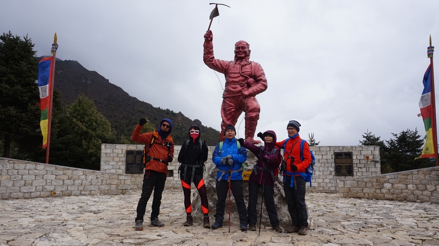 Group of hikers posing happily in front of a large mountaineering statue.