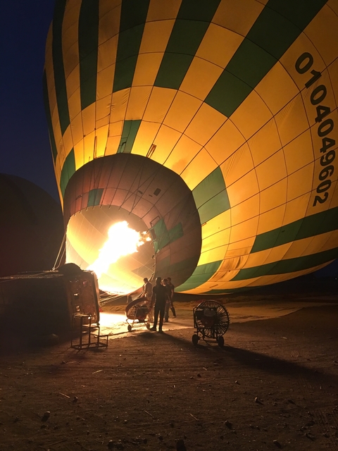       Preparation of a hot air balloon with flame visible at dawn or dusk.
  