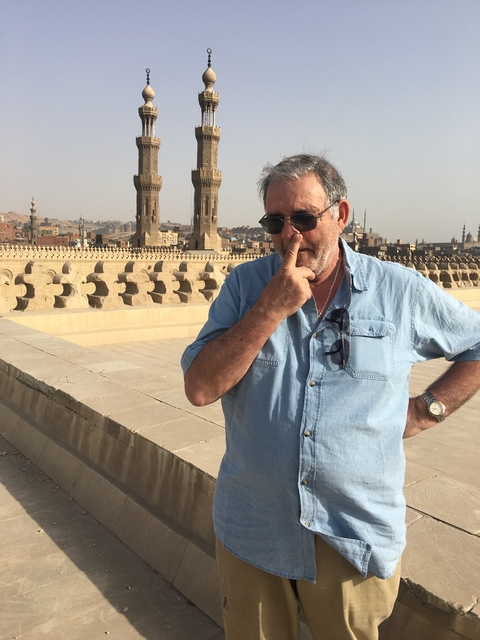       Man standing on an ancient structure with cityscape in the background.
  