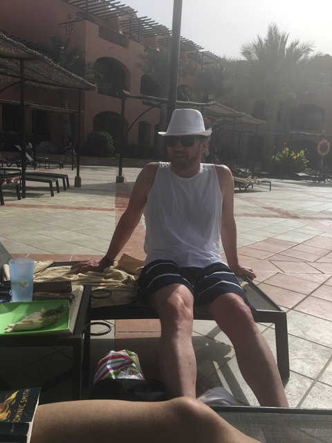       Man sitting by a poolside wearing a sunhat and sunglasses.
  