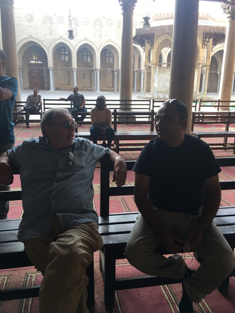       Two men sitting on a bench indoors with a spacious background.
  