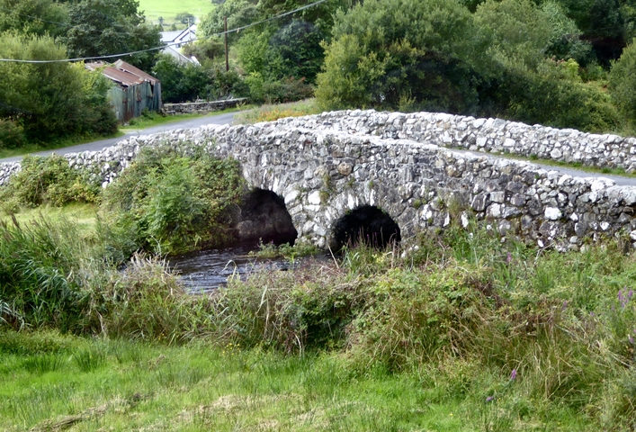       Stone bridge over a small stream in a lush area.
  