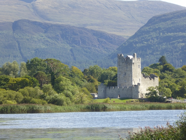 Castle with mountains in the background, near a lake.