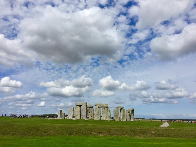 Stonehenge in a grassy field with visitors in the distance.