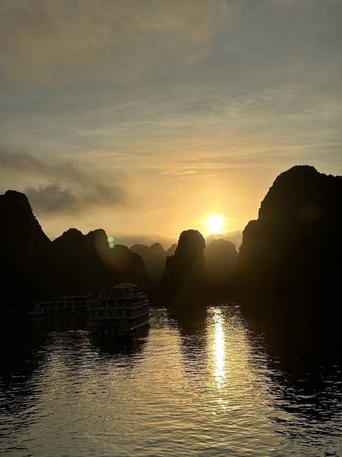 Sun setting behind limestone karsts reflected in the water.
