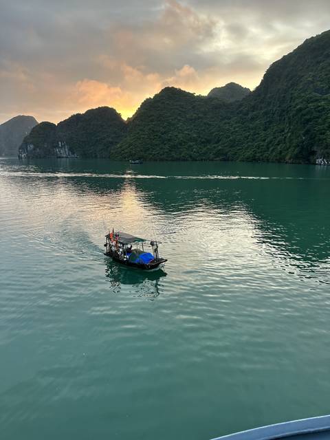 Fishing boat on calm waters surrounded by green karsts.