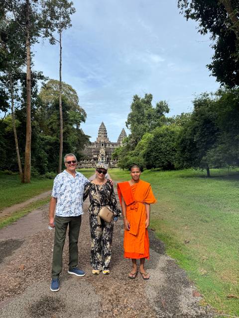       Three people, including two in traditional attire, at Angkor Wat.
  