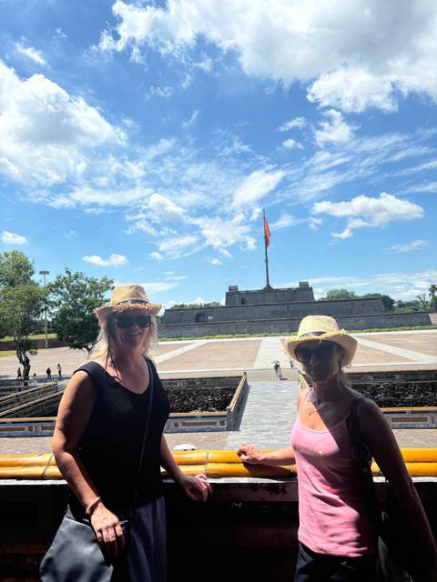       Two women in sunhats posing outside with a flag in the background.
  