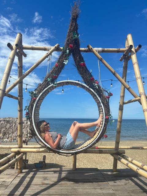 Woman posing inside a decorative circular swing structure by the beach.