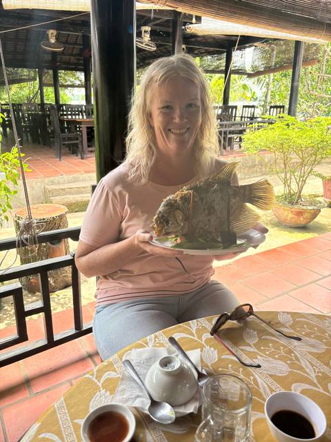       Woman holding a large fish dish at a restaurant table.
  