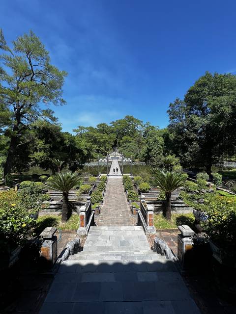 Stone bridge surrounded by greenery and ornate pillars.