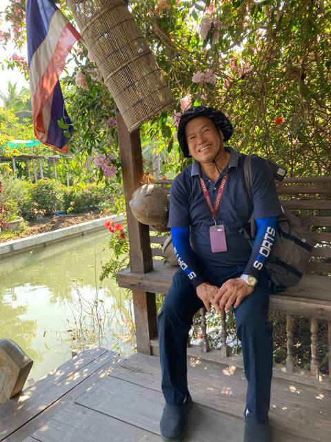 A man sitting on a bench with pink flowers and a canal.