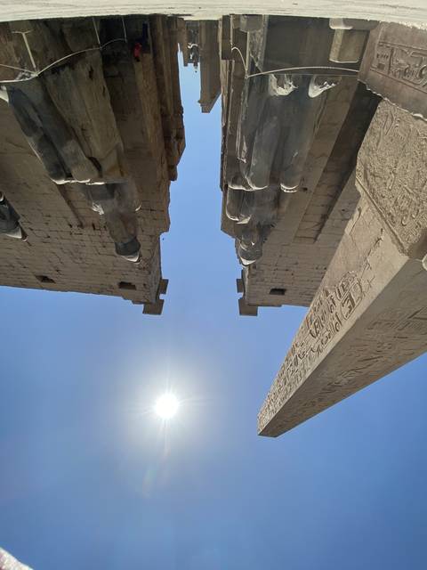       Ancient stone structures and sun disc in a historical site.
  