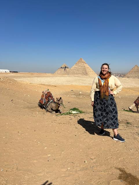       Tilted image of a person posing with a camel and pyramids.
  