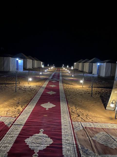 Desert camp with tents and a red carpet pathway at night.