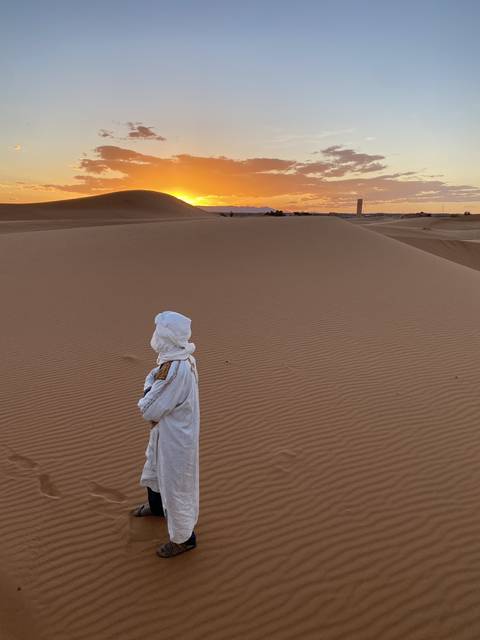 Person in traditional attire standing in a desert at sunset.