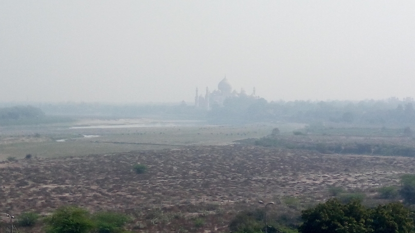 A distant view of the Taj Mahal through a hazy sky.
