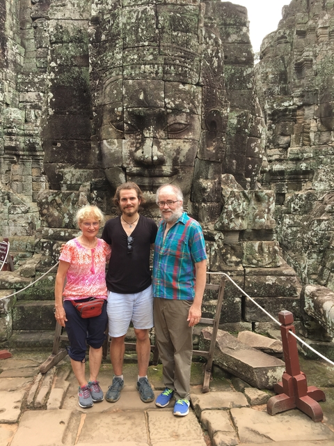 Three people standing in front of a stone structure with a carved face.