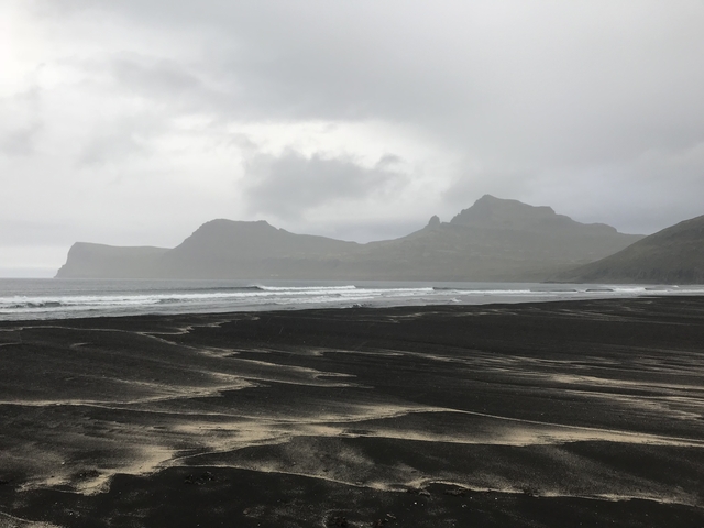 Dark sandy beach with waves and overcast sky.