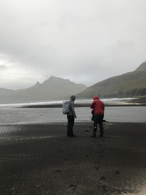 People wearing raincoats on a beach with mountains in the background.