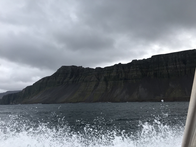 Boat view of rugged cliffs under a cloudy sky.