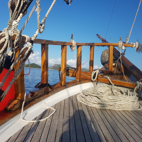Deck of a wooden ship with ropes and blue sea in the background.