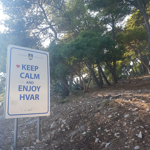       Sign reading 'Keep Calm and Enjoy Hvar' near trees.
  