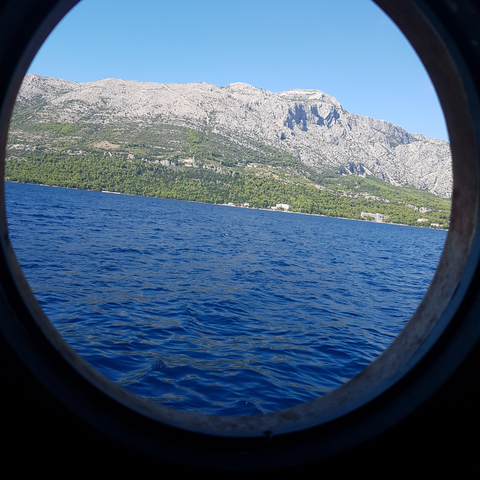       View of the sea and mountains through a circular window.
  