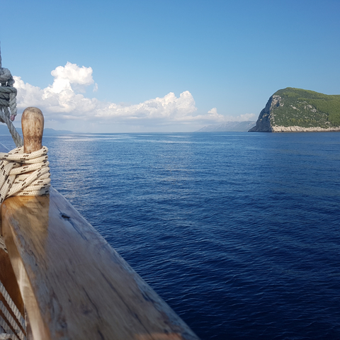 View of the sea with a wooden deck railing and a distant mountain.