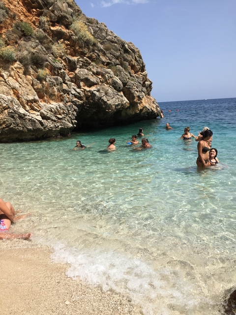 Clear water beach with people swimming and a cave nearby.