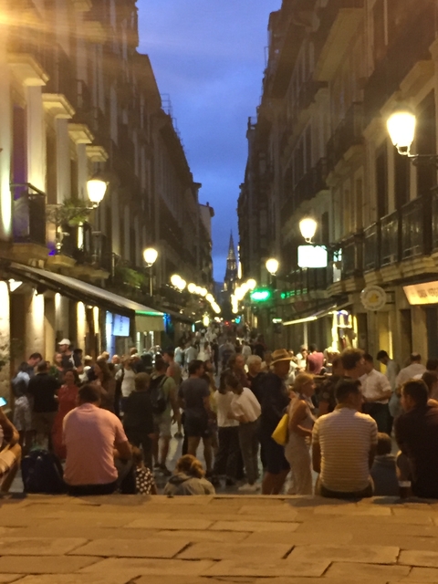       Nighttime bustling street scene with people and illuminated surroundings.
  