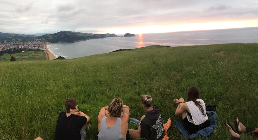       People sitting on a hill enjoying a sunset view over the ocean.
  