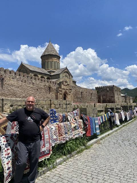 Man posing near traditional textiles and ancient structure.