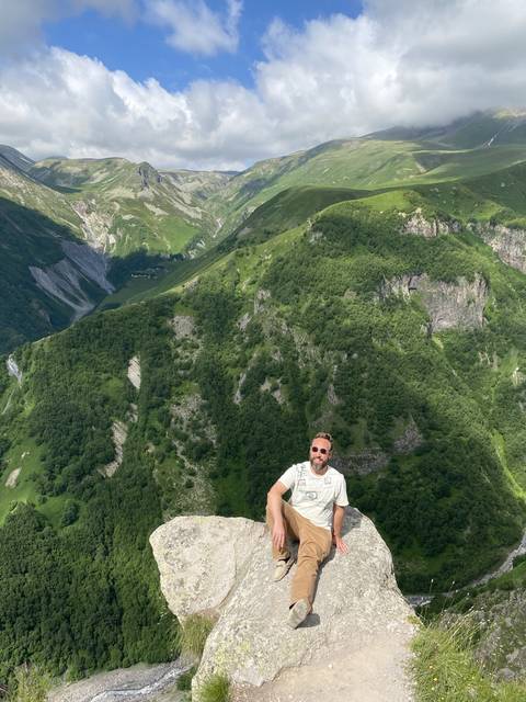       Man sitting on a rock with a valley view.
  