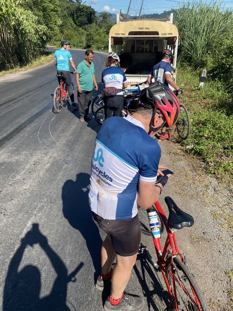       Cyclist using a smartphone on a road with other cyclists in the background.
  
