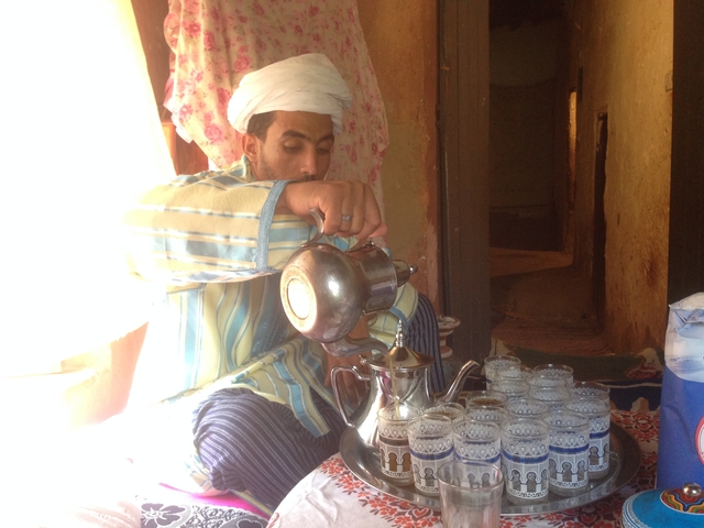       Man pouring tea into a glass placed on a tray.
  