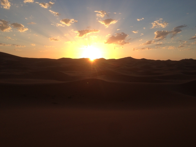       Sun setting over rolling sand dunes in the desert.
  