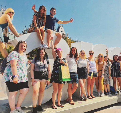 Group of people posing in front of a large white sign in an urban area.