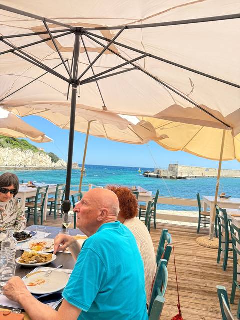       Seaside dining area with people seated, umbrellas, and ocean view.
  
