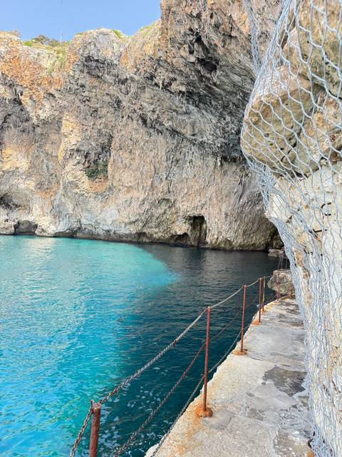       Coastal path and crystal clear blue water by rocky cliffs.
  