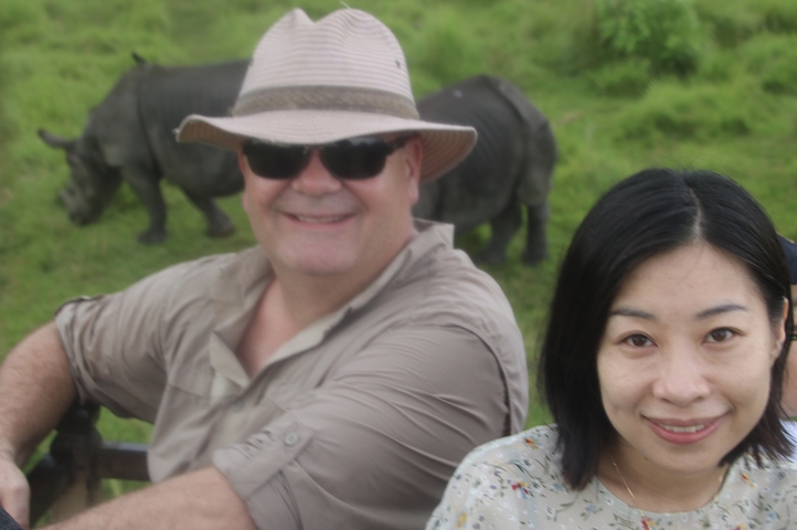 Couple smiling with rhinos in the background.