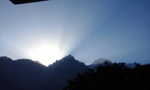 Sunrays over mountains with a silhouette of trees.