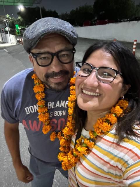 Two people smiling and wearing flower garlands.
