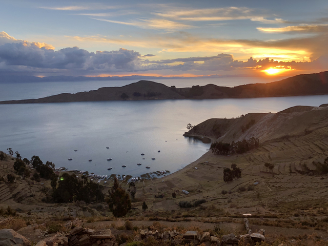 Sunset over a lake with boats and hills.